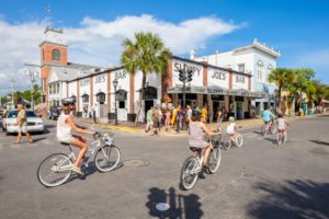 People riding bikes down Key West street next to Sloppy Joe's Bar.