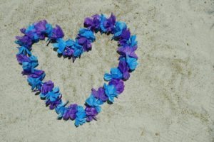 Flower leis made of blue and purple flowers in shape of heart on beach.